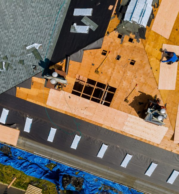 A roofer nailing shingles with air gun, replacing roof cover protection being applied, apartment development