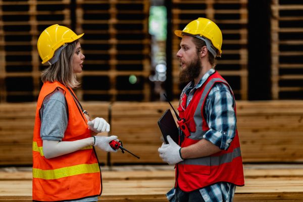 workers carpenter wearing safety uniform and hard hat working and checking the quality of wooden products at workshop manufacturing. man and woman workers wood in dark warehouse industry.