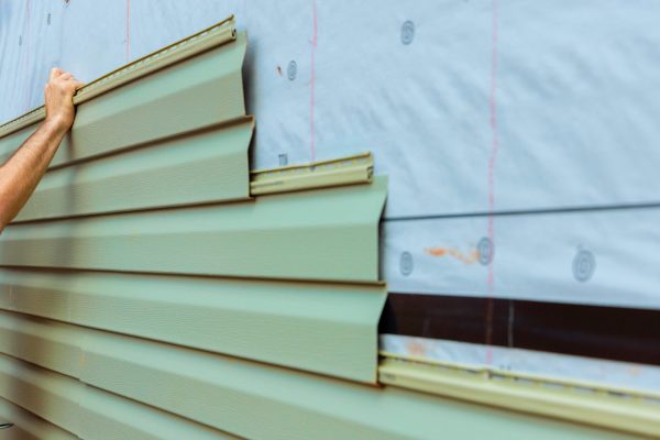 Construction worker carefully lays green siding on building exterior while ensuring proper fit.